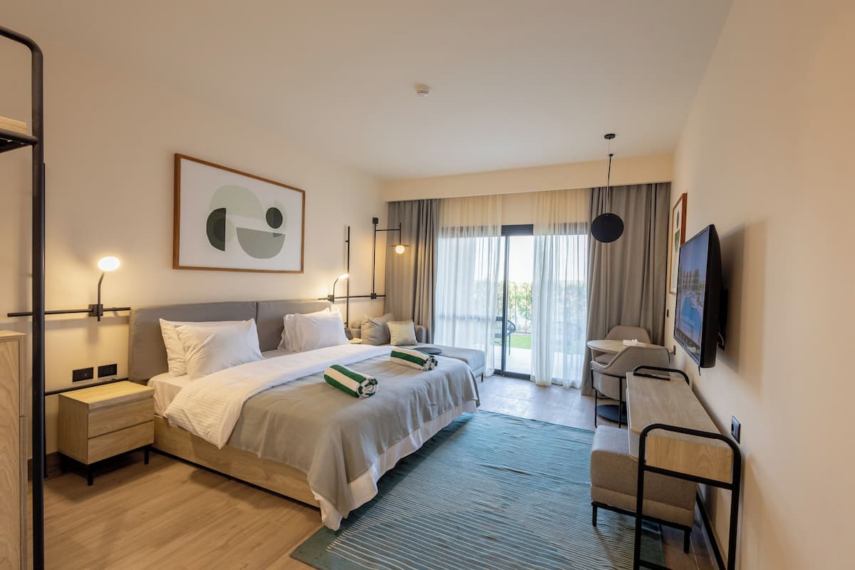 A modern hotel room with a large bed, bedside tables, a desk, and a TV.