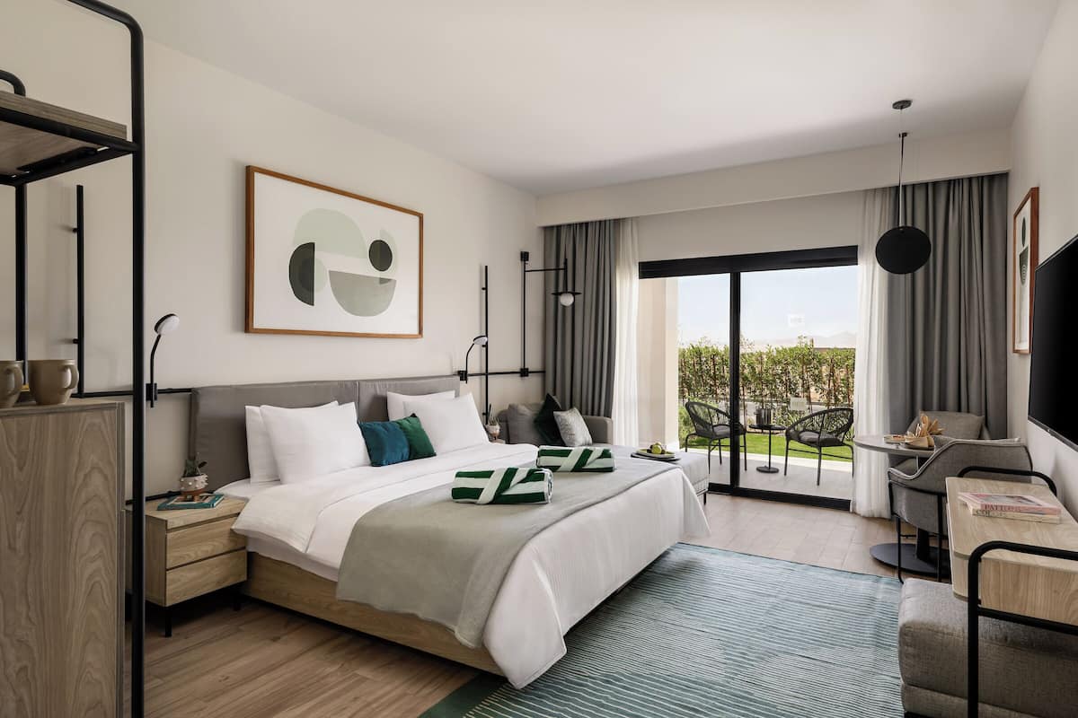 A modern hotel room with a large bed, a desk, and a balcony with a view.
