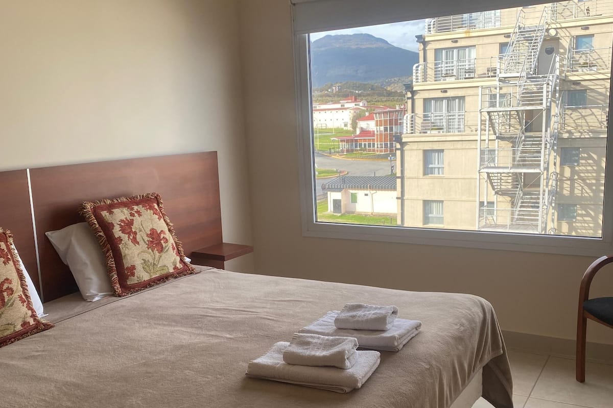 A hotel room with a large bed, a view of buildings and mountains, and a window with a view of a cityscape.