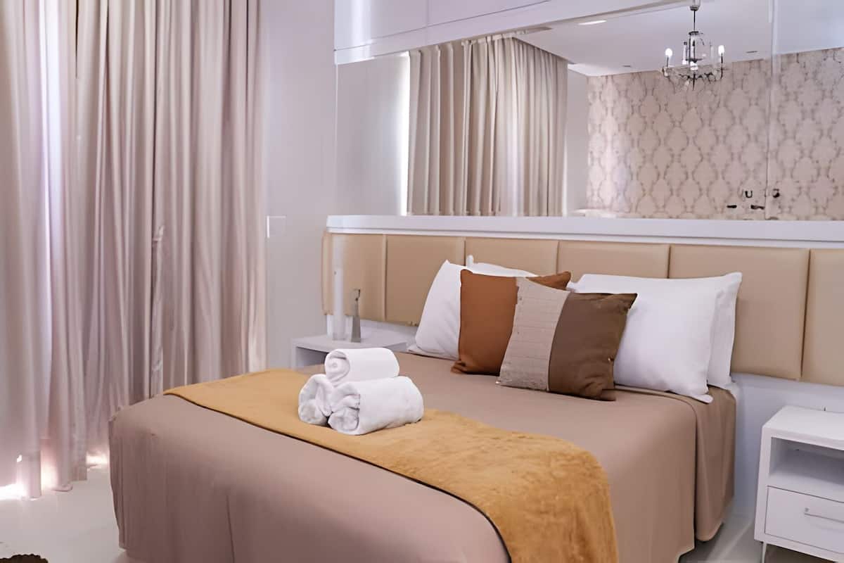 A modern hotel room with a large bed, a bedside table, a nightstand, and a mirror above the bed.