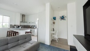 Een moderne woonkamer met een grijze bank, een televisie en een keuken met witte kasten en een aanrecht.