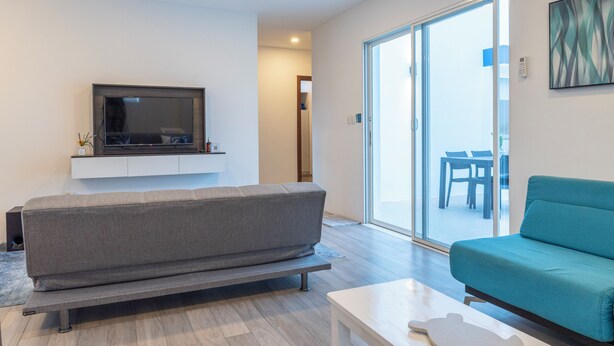 Een moderne woonkamer met een grijze bank, een witte salontafel en een flatscreen televisie aan een witte muur.