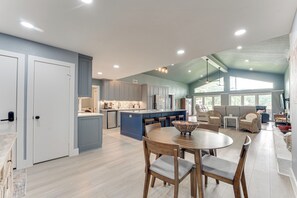 Un'ampia cucina con isola centrale, una zona pranzo con tavolo rotondo e un soggiorno con divani e un'ampia finestra.