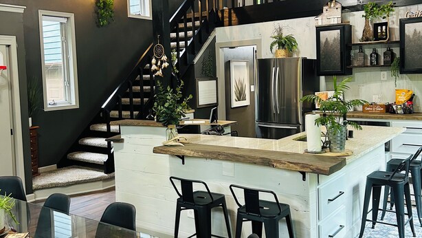 Una cocina moderna con una isla central, taburetes negros y una zona de comedor con mesa de vidrio.