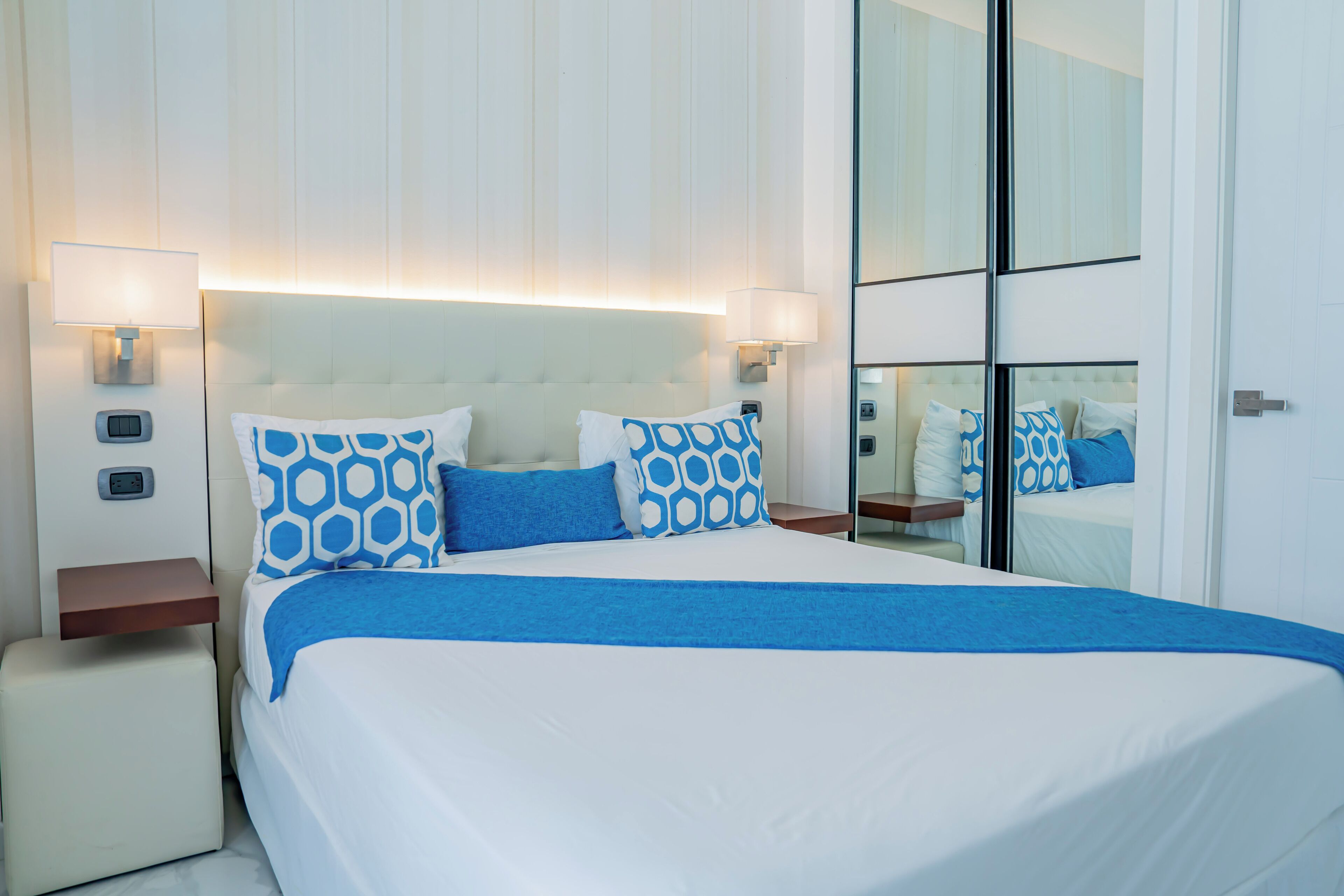 Une chambre d’hôtel avec un grand lit, deux tables de chevet, une petite table et un miroir.