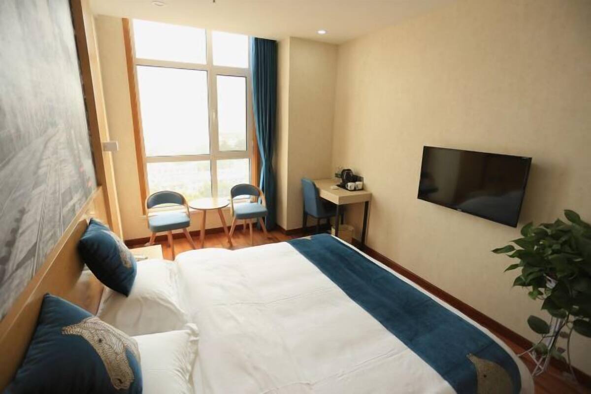 A hotel room with a bed, a desk, a chair, a TV, and a window with curtains.