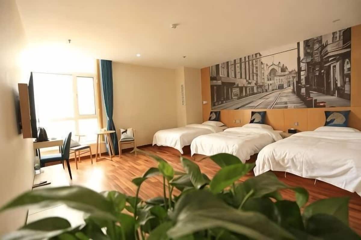 A hotel room with three beds, a desk, a chair, and a large window.