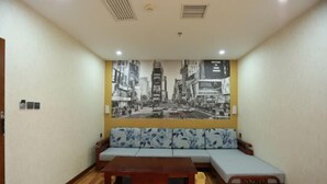 Una habitación con un sofá, una cama pequeña, una mesa de centro de madera y una obra de arte en la pared que representa un paisaje urbano.
