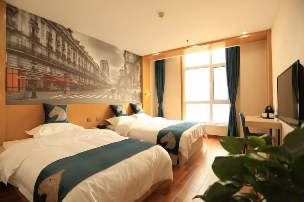 A hotel room with two beds, a large cityscape mural, a desk with a chair, and a television.