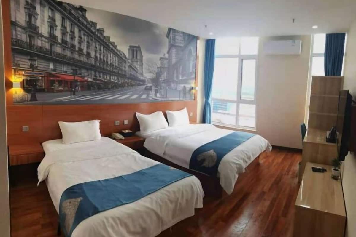 A hotel room with two beds, a large cityscape mural, a wooden floor, a desk, and an air conditioning unit.