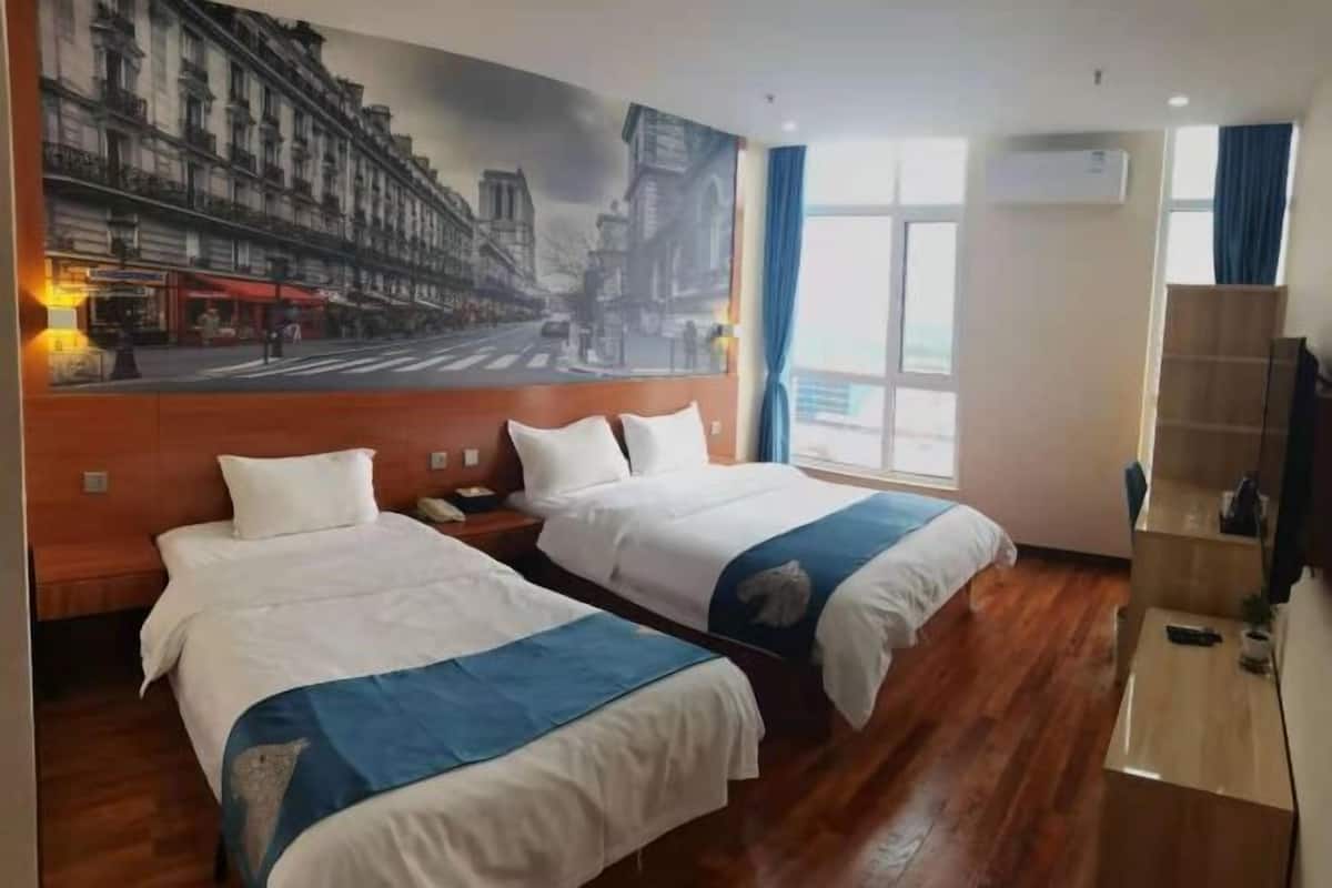 A hotel room with two beds, a large cityscape mural, a wooden floor, a desk, and a TV.