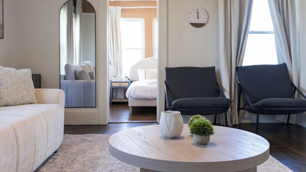 Ein modernes Wohnzimmer mit einem runden Couchtisch, einer Couch und zwei Sesseln. Auf dem Tisch steht eine kleine Topfpflanze.