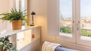 Une pièce avec une fenêtre, une plante en pot, une lampe et une vue sur le paysage urbain.