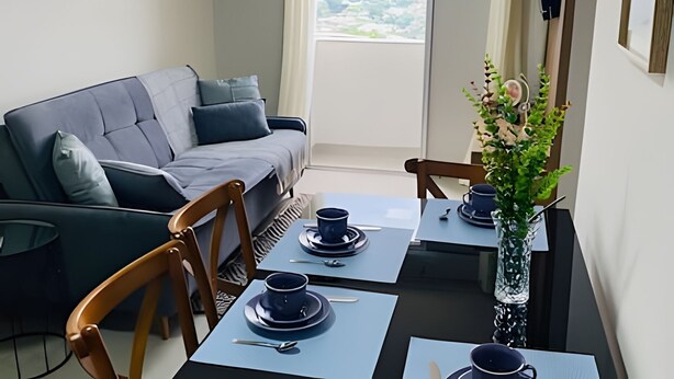 Una sala de estar moderna con un sofá gris, sillas de madera, una mesa de comedor con vajilla azul y una planta decorativa.