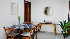Un comedor con una mesa dispuesta para cuatro personas, rodeada de sillas de madera con asientos acolchados. Un espejo redondo cuelga en la pared sobre la mesa.