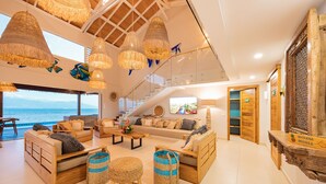 A spacious living area with a large window overlooking the sea, a staircase, and a wooden reception desk.