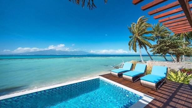 A poolside area with lounge chairs, a wooden deck, and a view of the ocean and mountains.