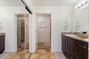 Un baño moderno con mampara de vidrio, tocador con lavabo y un espejo grande.