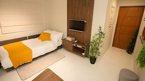 A modern bedroom with a bed, a TV mounted on a wooden panel, a desk, and a potted plant. - APTO decorado 5 hospedes AC e piscina (Foz do Iguaçu)
