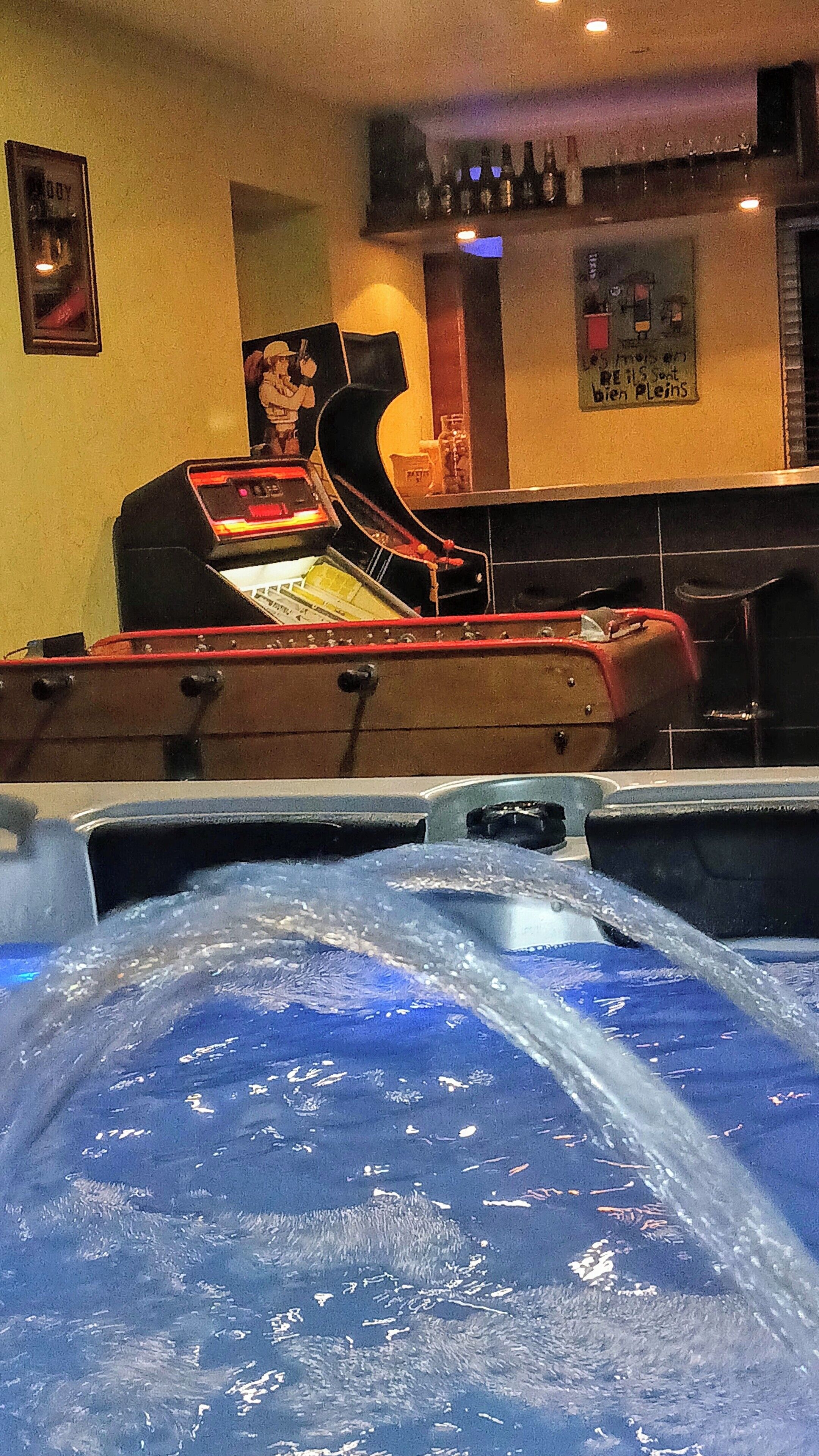 A bar area with a pool table, a jukebox, and a poster on the wall.