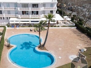 Une piscine bordée d’un palmier, entourée d’une zone pavée et d’un bâtiment doté de balcons.