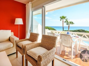 Ein Balkon mit Korbstühlen, einem weißen Tisch und Blick auf das Meer.
