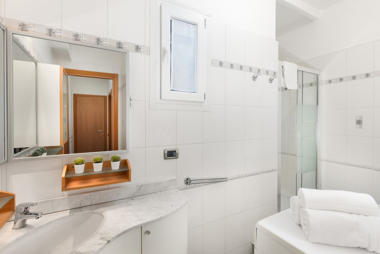 A bathroom with a marble sink, a mirror, a small window, a towel rack, and a glass shower enclosure.