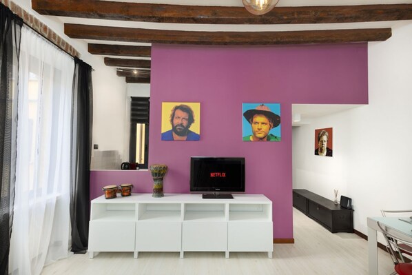Una sala de estar con un mueble blanco para entretenimiento, un televisor de pantalla plana y dos retratos enmarcados sobre una pared morada.