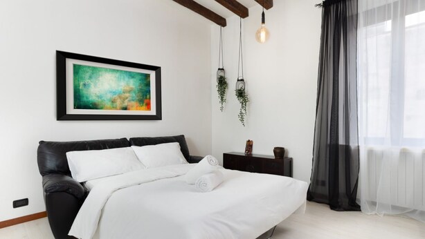 A modern bedroom with a black leather bed, white bedding, a framed abstract painting, hanging planters, and sheer curtains. - LECCO, 20 - In the heart of the Rainbow District. (Milan)
