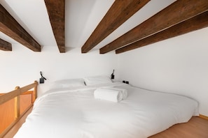 A bedroom with a wooden ceiling, white bedding, and a wooden railing.