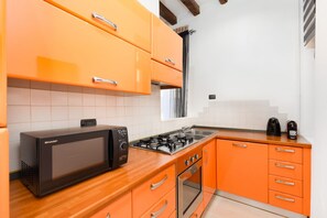 A kitchen with orange cabinets, a black microwave, a gas stove, and a coffee maker. - LECCO, 20 - In the heart of the Rainbow District. (Milan)