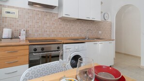 A modern kitchen with a wooden countertop, stainless steel appliances, a washing machine, and a dining area with a table set for two. - Don Leandro's House by Rentbeat (Civitavecchia)