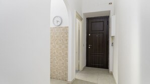 A hallway with a tiled floor, a clock on the wall, and a dark wooden door. - Don Leandro's House by Rentbeat (Civitavecchia)