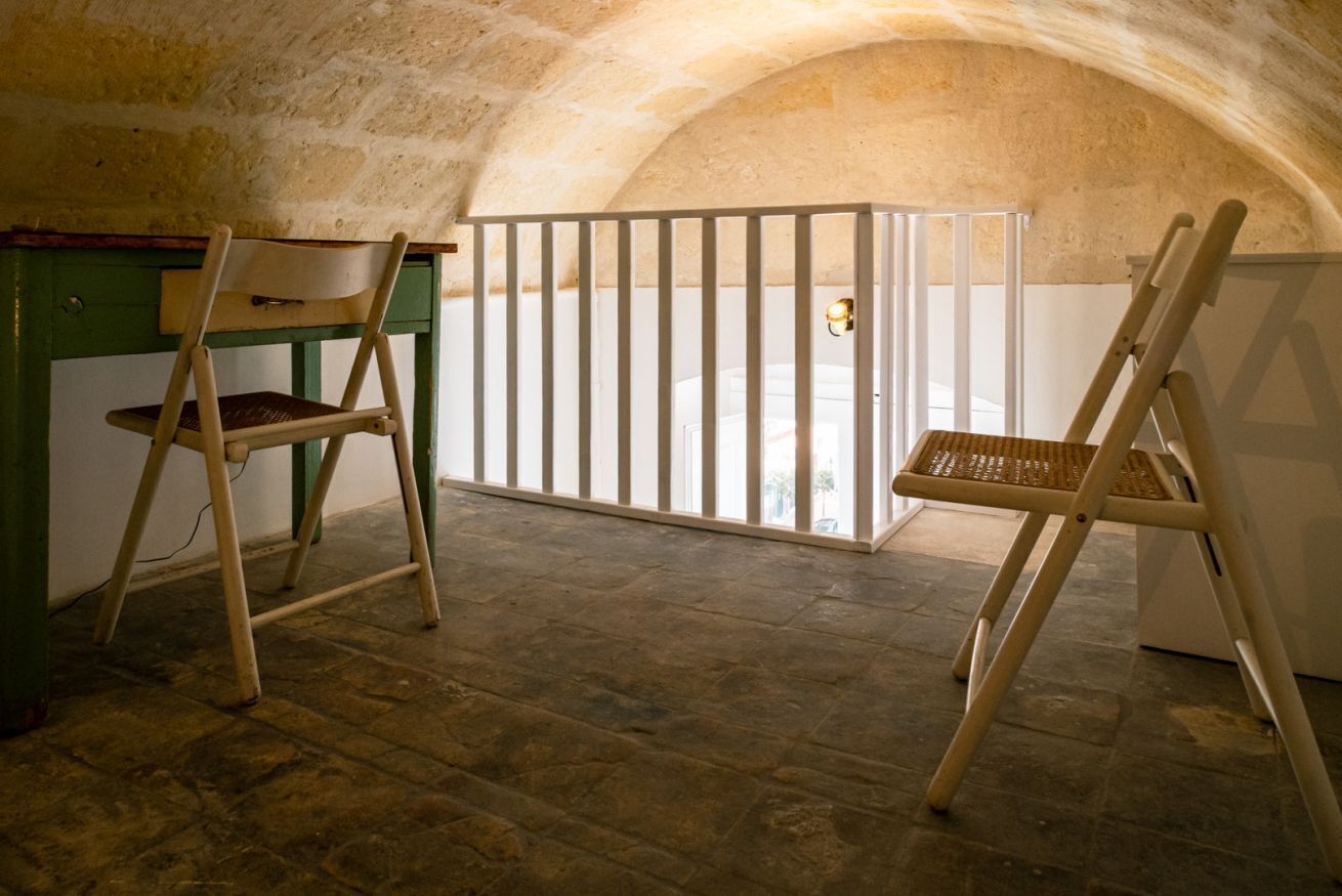A room with a stone wall, a wooden desk, two chairs, and a white gate.