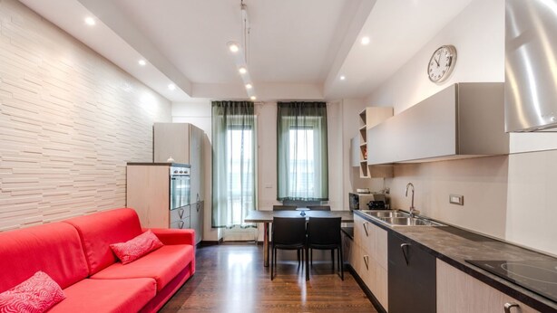 A modern kitchen with a dining area, a red sofa, and a clock on the wall. - Casa Peschiera by Rentbeat (Torino)