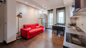A modern apartment with a red sofa, a dining area, a kitchen with a built-in stove, and a white brick wall. - Casa Peschiera by Rentbeat (Torino)
