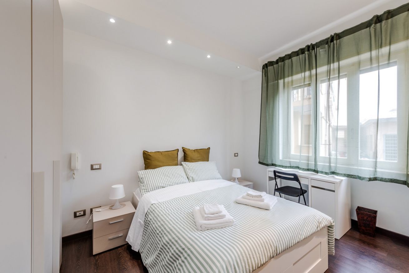 A bedroom with a bed, bedside tables, a chair, and a window with curtains.
