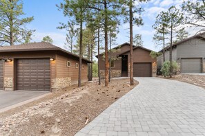 Two-story house with a brown exterior and stone foundation, set amidst a landscaped area with pine trees and shrubs.