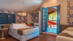 Ein Schlafzimmer mit Bett, kleinem Tisch und Kleiderschrank. Ein Fenster mit offener Tür führt nach draußen.