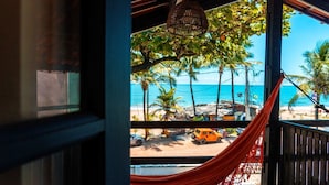 Une vue sur la plage depuis un porche abrité, avec un hamac, des palmiers et une voiture garée.