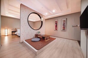 A modern hotel room with a bed, a small seating area with a table and cushions, a large mirror, and artwork on the walls. - K. Y. Hotel (Liuzhou)