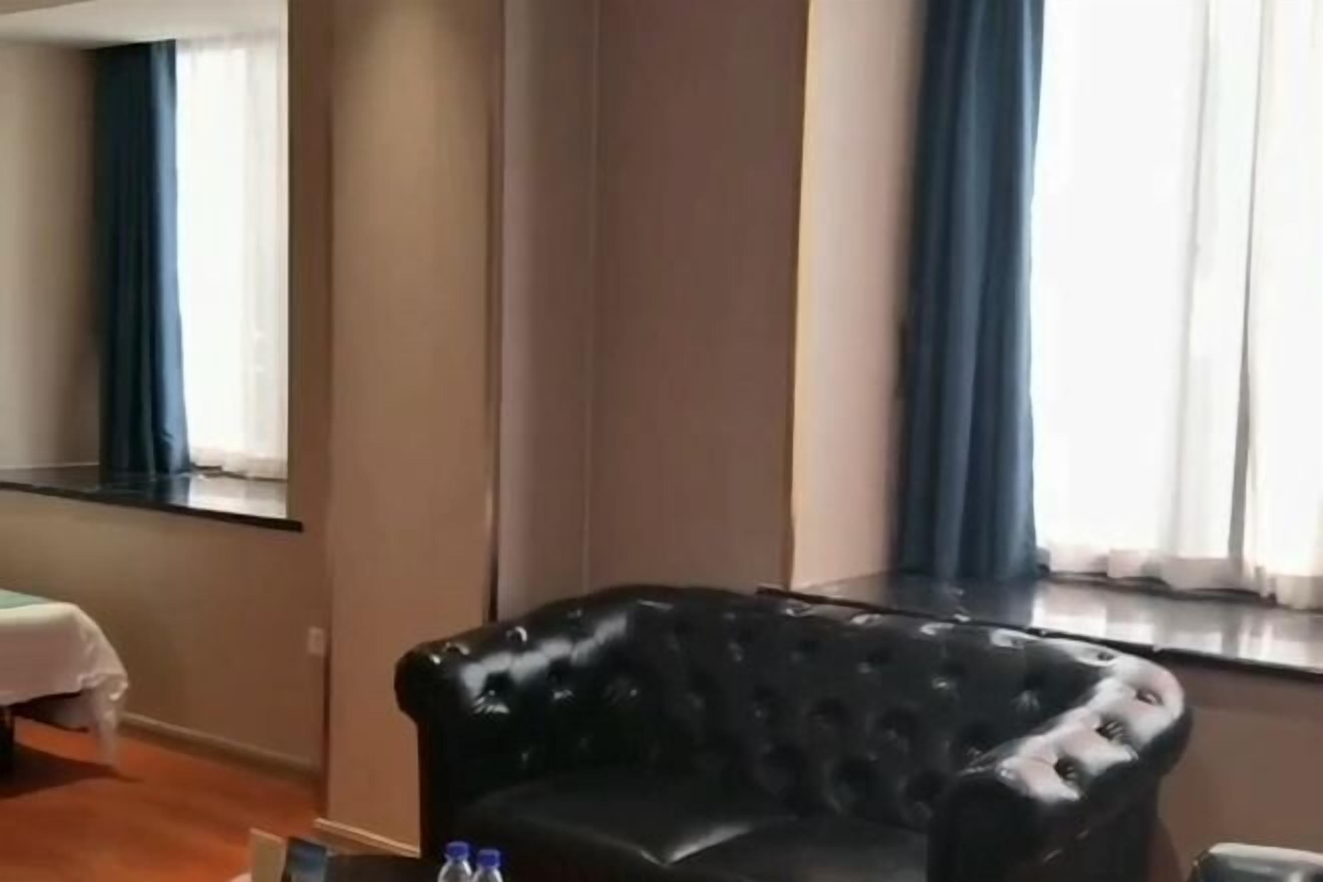 Ein Zimmer mit einem schwarzen Ledersessel, einem Bett mit weißer Bettdecke und einem Fenster mit blauen Vorhängen.