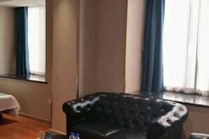 A room with a black leather armchair, a bed with a white bedspread, and a window with blue curtains. - K. Y. Hotel (Liuzhou)