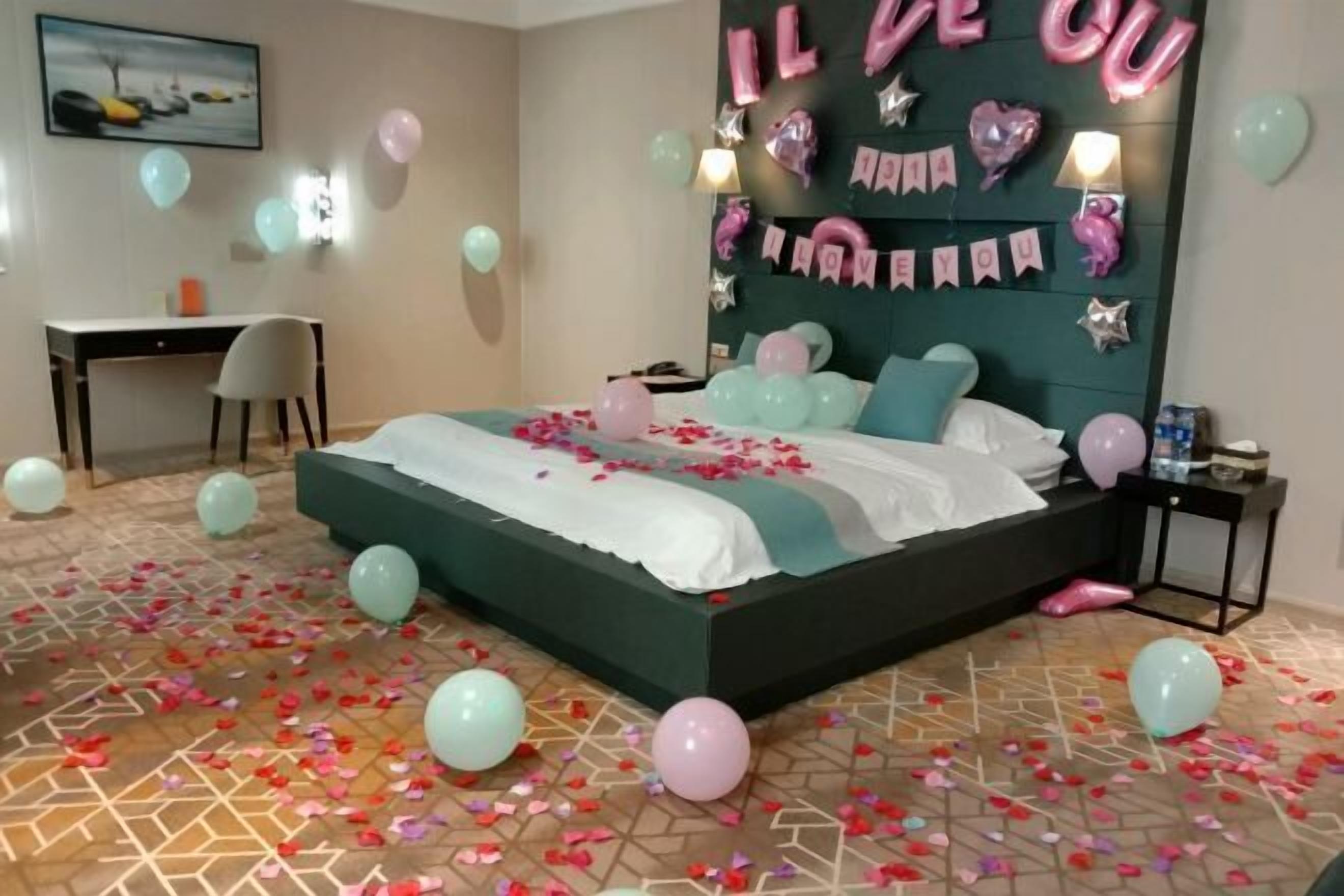 A bedroom with a bed, a desk, and a chair. There are balloons and a wall decoration with the text "IL BEU".