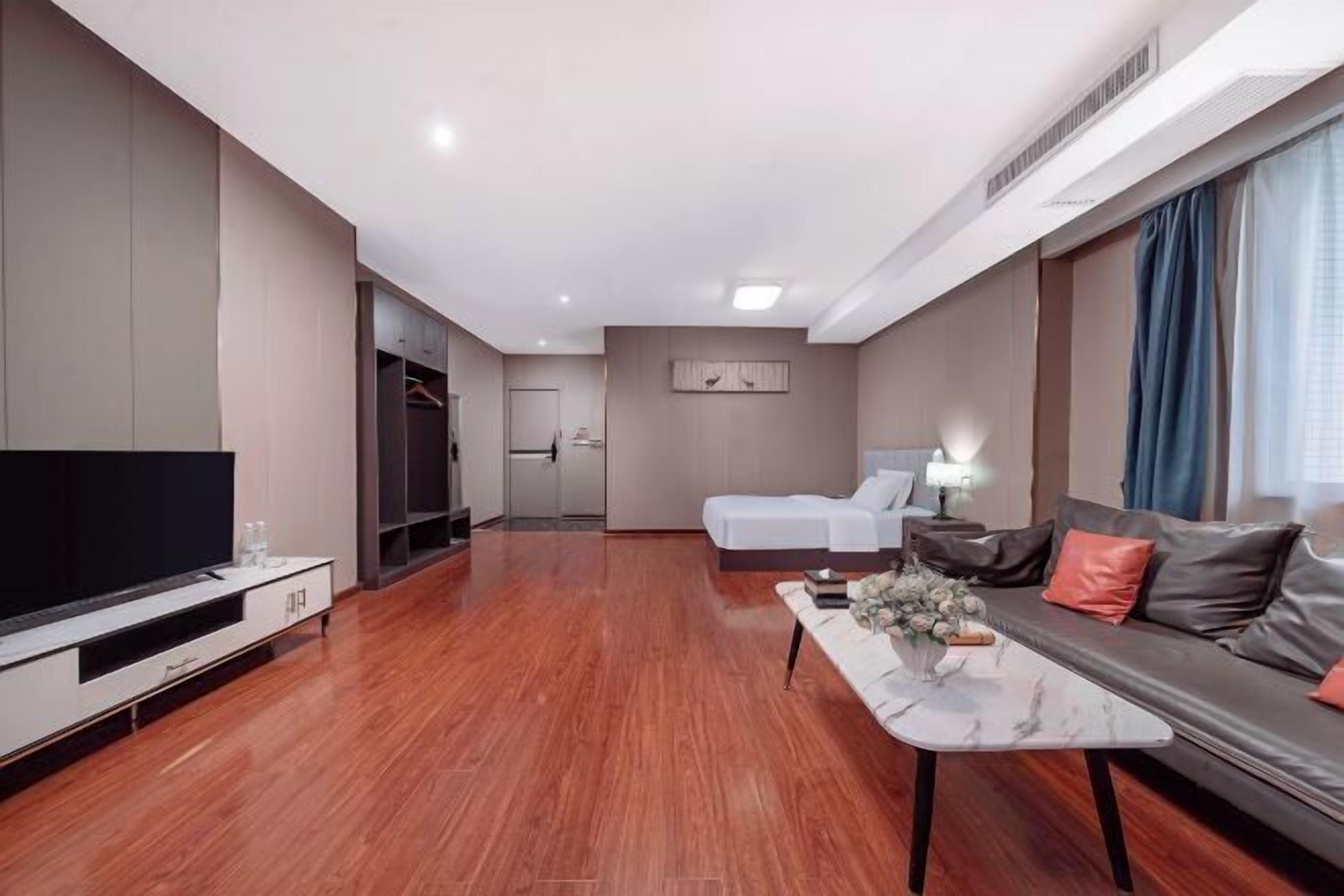 A modern hotel room with a flat-screen TV, a sofa, a bed, a dining table, and a walk-in closet.