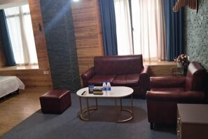 A cozy room with a wooden wall, a red leather sofa, a small round table with a book and bottles, and a window with curtains. - K. Y. Hotel (Liuzhou)