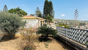 Zona residencial con una casa, una valla metálica y vista a un pueblo al fondo.