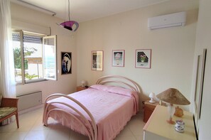 Een slaapkamer met een bed, een stoel, een tafel met een lamp en een raam met jaloezieën.