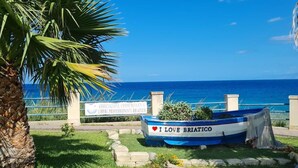 Une scène côtière avec une enseigne indiquant « Associazione Commerciali e Liberi Professionisti Briatico » et un bateau sur lequel on peut lire « J’AIME BRIATICO ».
