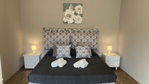 Un lit bien fait, recouvert d’une couvre-lit sombre et agrémenté de rideaux assortis, flanqué de deux tables de chevet avec des lampes, et un tableau floral au-dessus du lit.